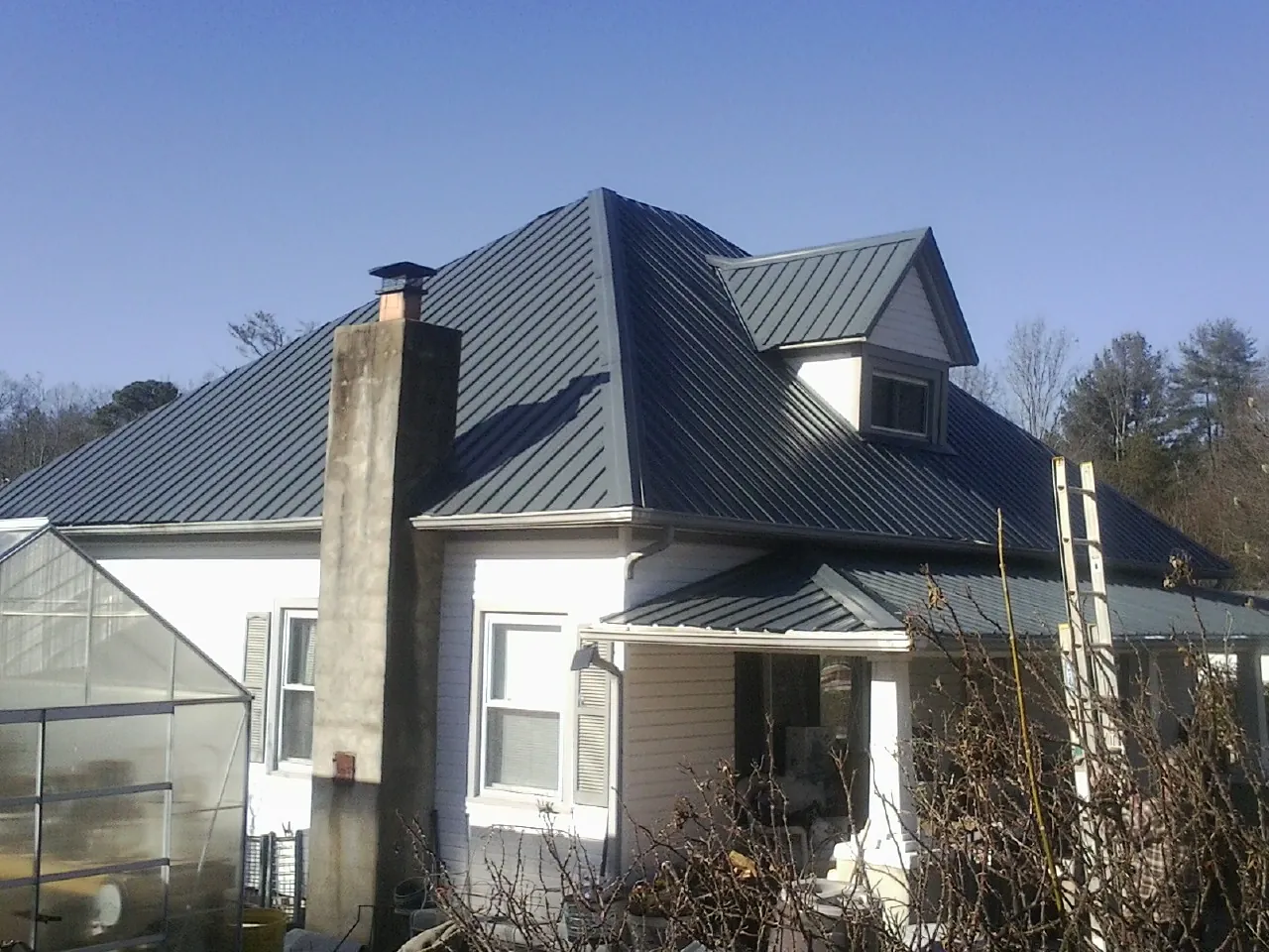 Dark blue standing seam metal roof on a white farmhouse with dormer — Slate & Tile Roof Repair by Roofing Brothers in Grand Prairie