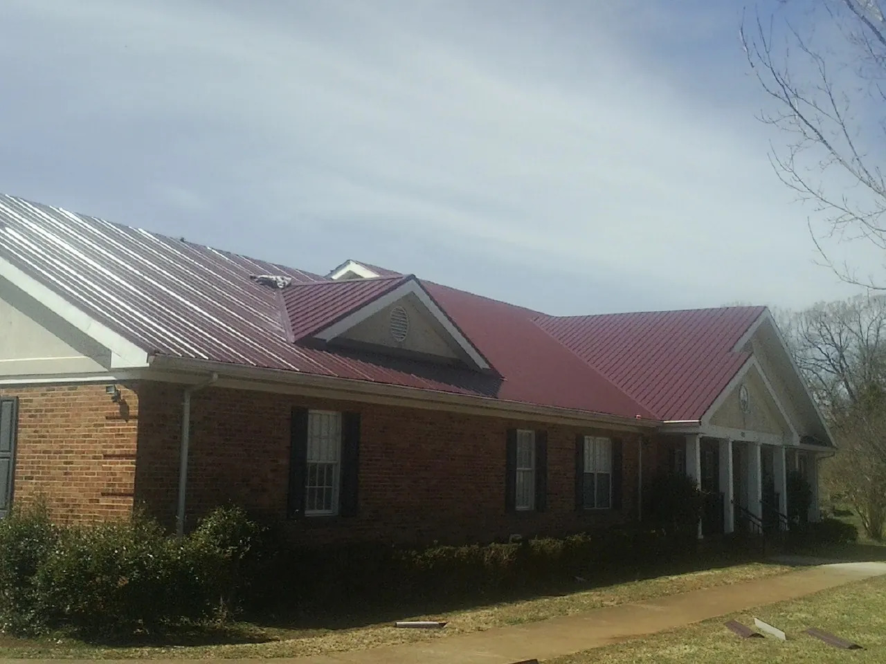 Red metal roof with gabled entries on a long brick building, from a Hail Damage Roof Repair job in Grand Prairie
