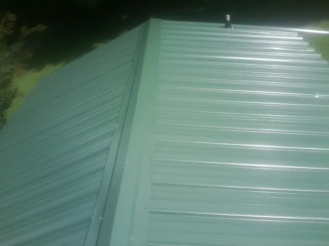 New green metal panels meeting at the ridge of a roof — Flat Roof Repair work by our crew in Grand Prairie