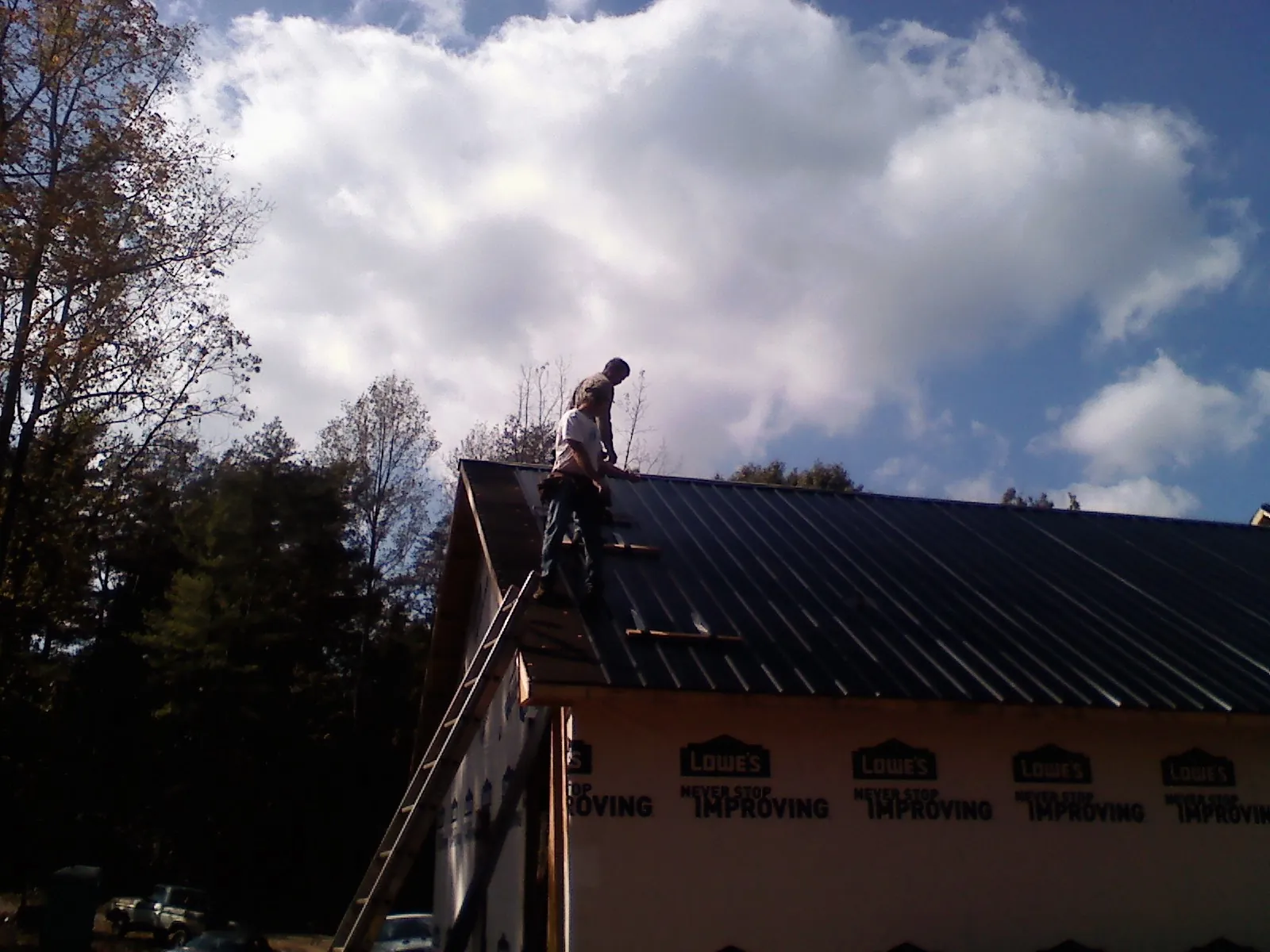 Roofer fastening dark metal panels high against a cloudy sky, from a Roof Inspection job in Grand Prairie