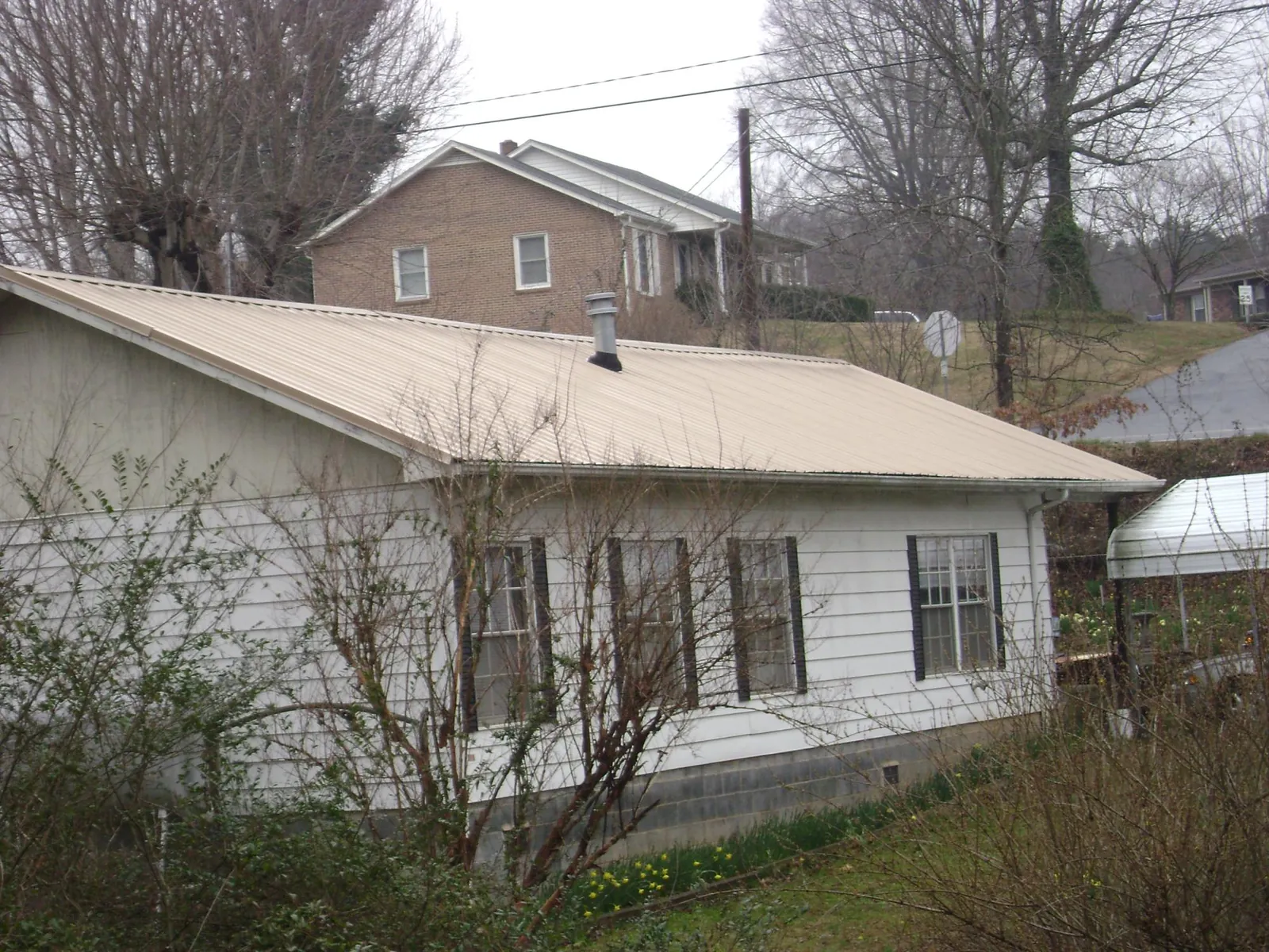 Tan metal roof on a white sided house set into a hillside — Commercial Roofing by Roofing Brothers in Grand Prairie