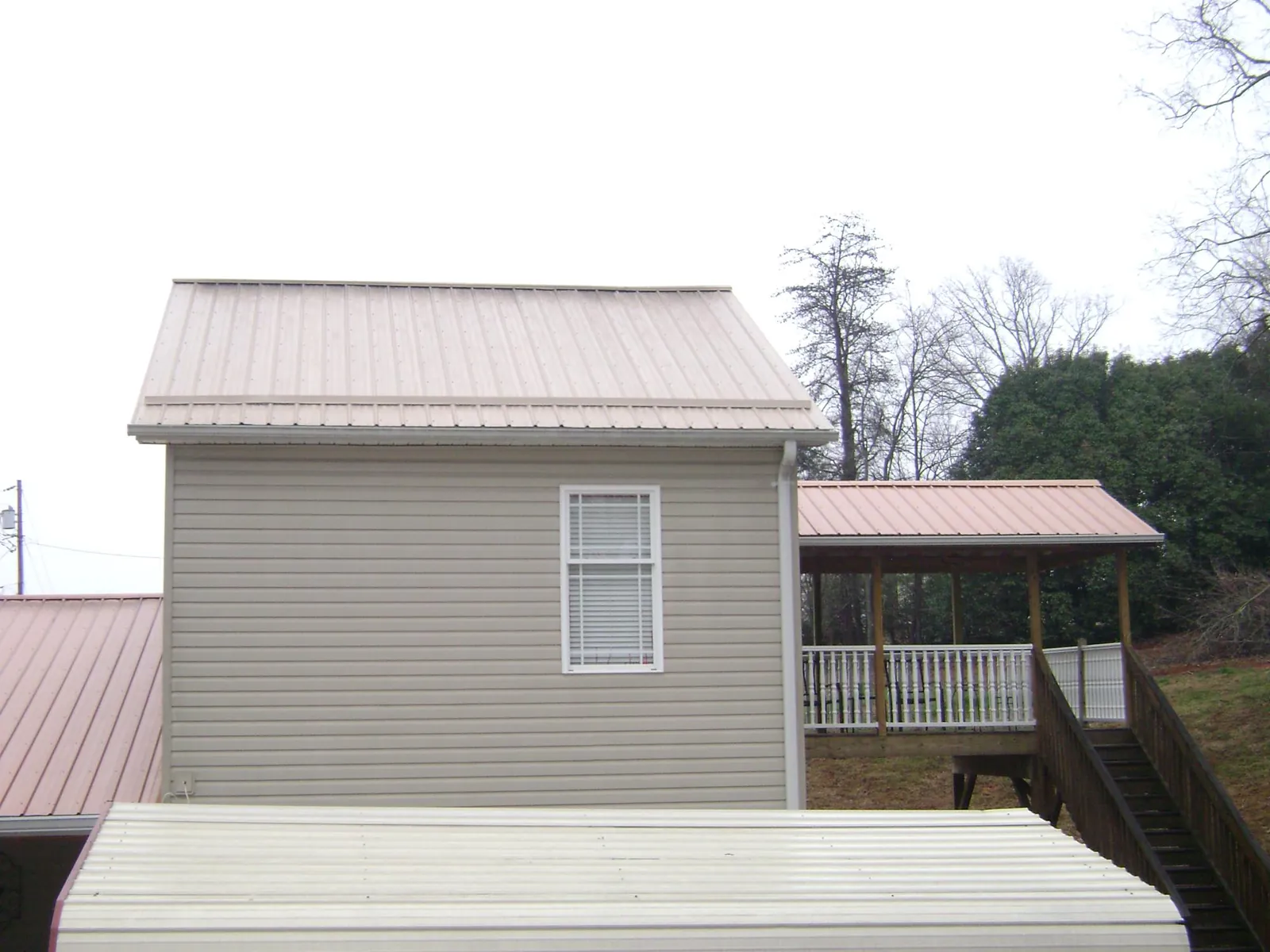 Tan metal roofs on a two story addition and attached porch, from a Roof Replacement job in Grand Prairie